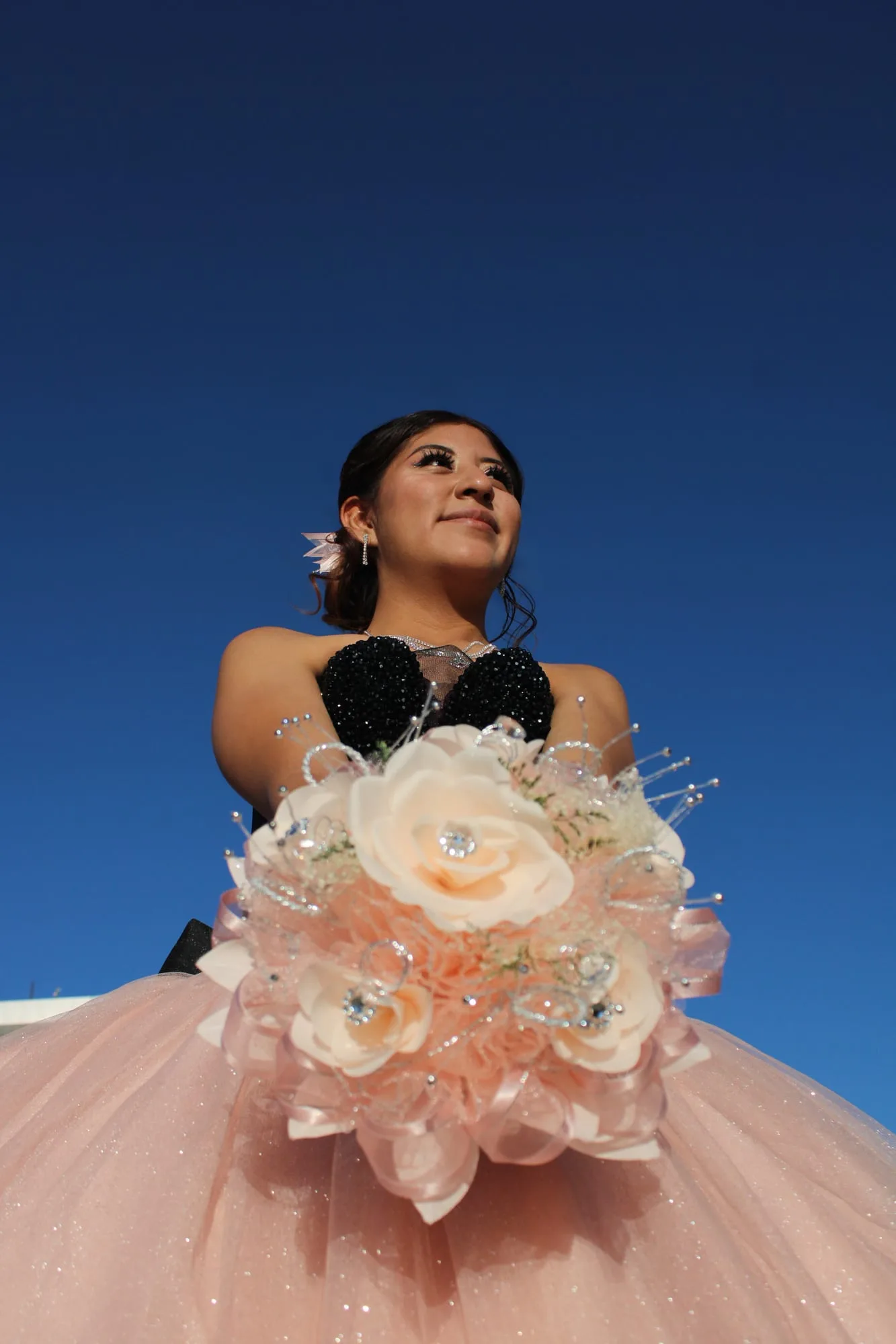 Quinceañera con vestido rosa y cielo azul de fondo